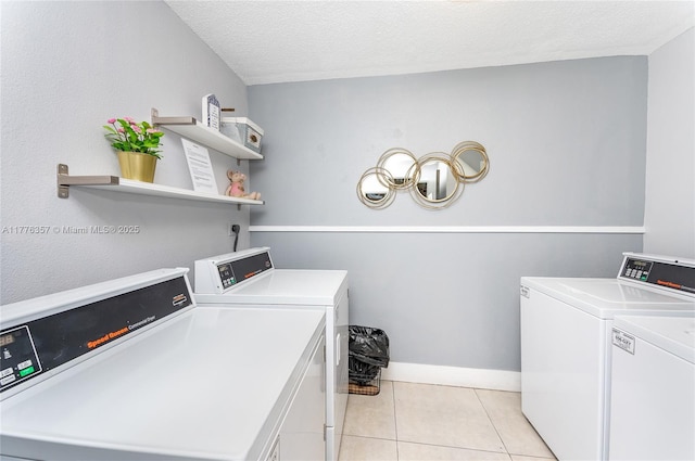 washroom with washing machine and clothes dryer, light tile patterned floors, baseboards, and a textured ceiling