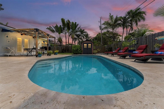 view of swimming pool with an outdoor structure, a patio, french doors, a fenced backyard, and a storage shed