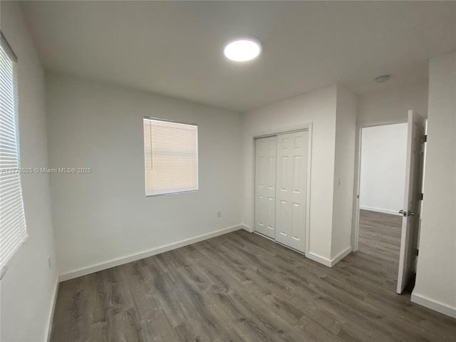 unfurnished bedroom with a closet, dark wood-type flooring, and baseboards