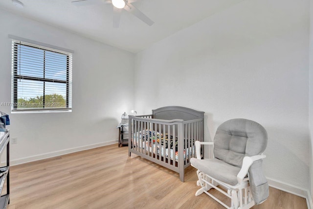 bedroom featuring baseboards, wood finished floors, ceiling fan, and a nursery area