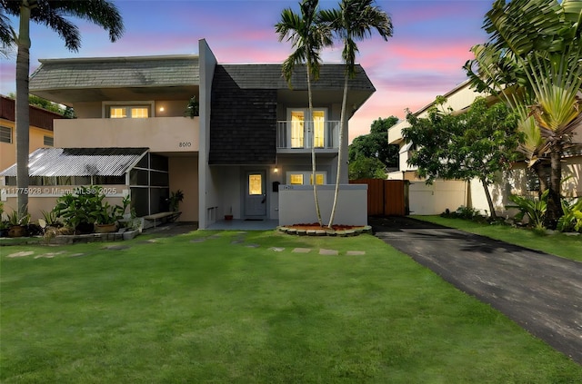 view of front of house with a front lawn, a balcony, stucco siding, mansard roof, and driveway
