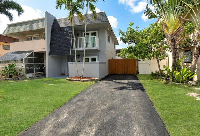 contemporary house with driveway, a front yard, roof with shingles, mansard roof, and stucco siding