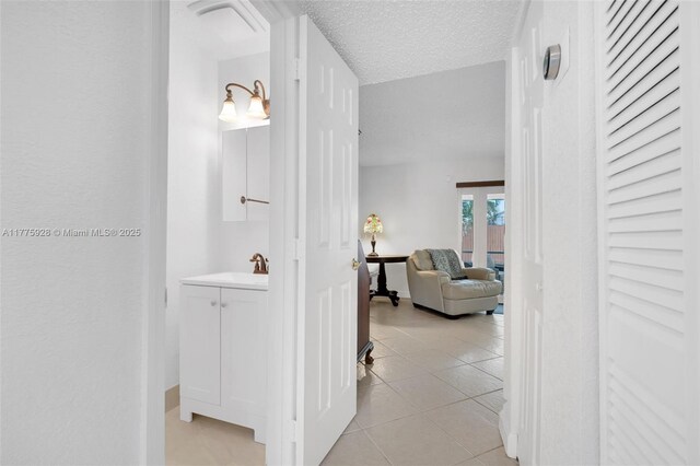 hall featuring baseboards, a sink, a textured ceiling, and light tile patterned flooring