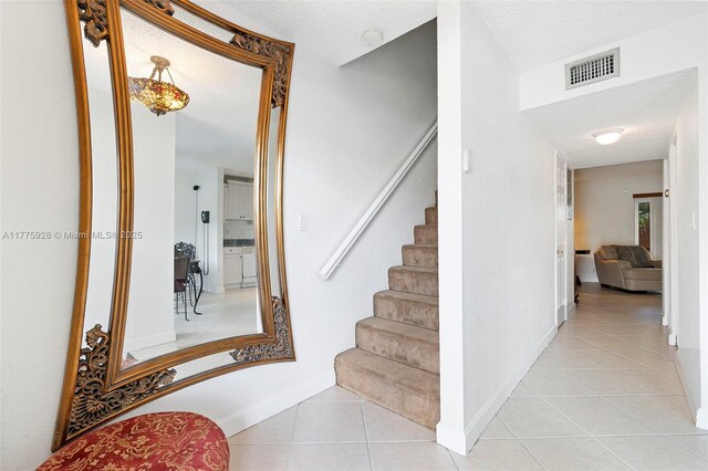 staircase featuring visible vents, baseboards, a textured ceiling, and tile patterned flooring