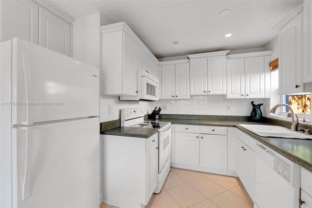 kitchen with dark countertops, a sink, white appliances, a textured ceiling, and white cabinetry