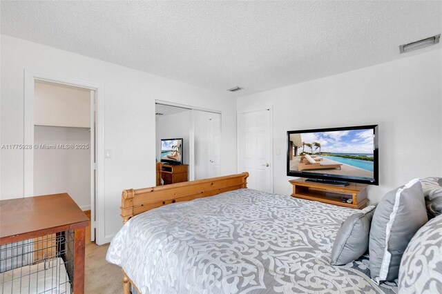 bedroom featuring a textured ceiling, light colored carpet, visible vents, and a closet