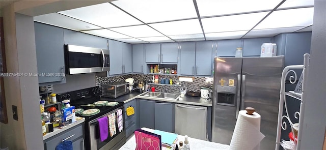 kitchen with decorative backsplash, a sink, gray cabinetry, stainless steel appliances, and a drop ceiling