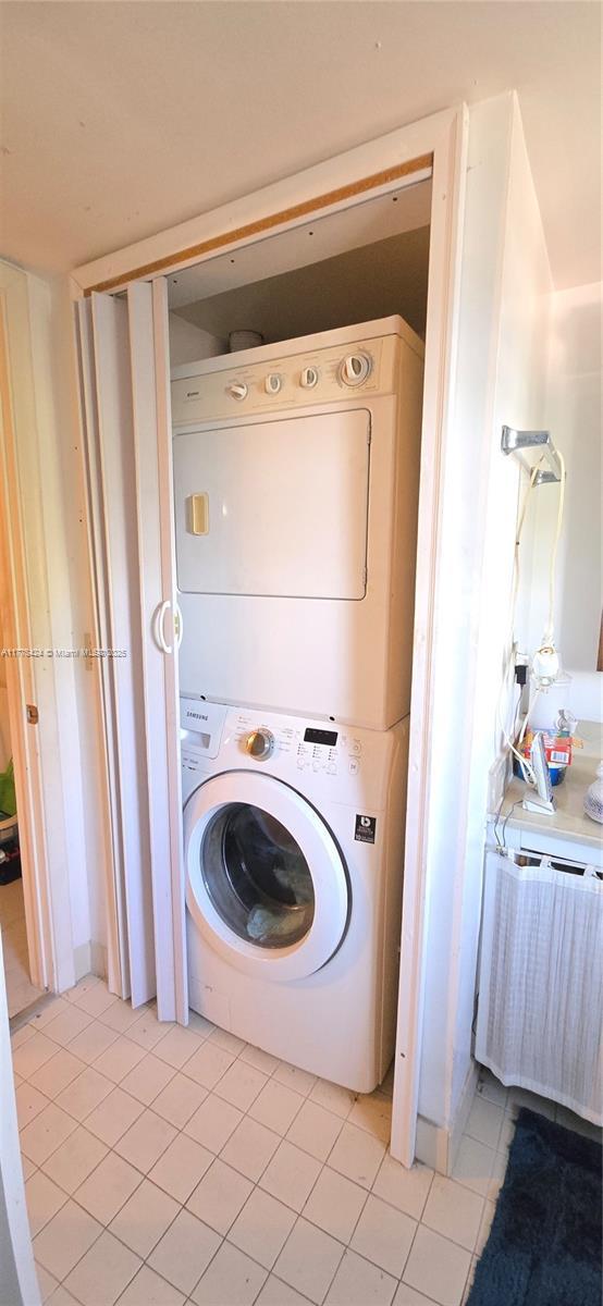 clothes washing area featuring light tile patterned floors, radiator heating unit, stacked washer / dryer, and laundry area