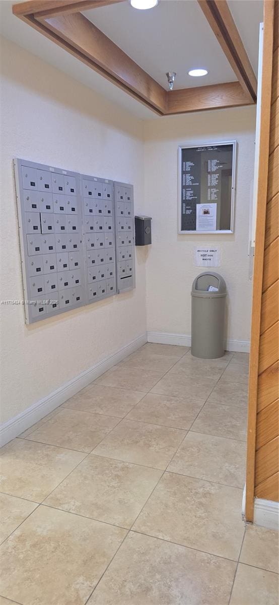 interior space featuring tile patterned floors, baseboards, a raised ceiling, and mail area