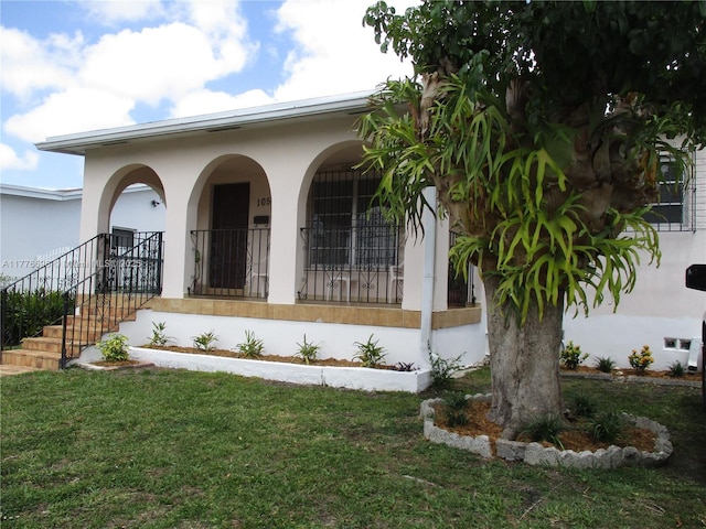 105 NW 32nd Pl, Miami, FL 33125 - view of exterior entry with a porch, a lawn, and stucco siding