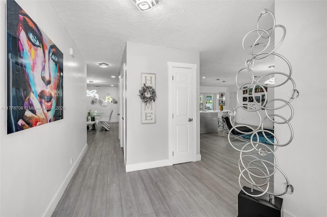 corridor featuring baseboards, a textured ceiling, and wood finished floors