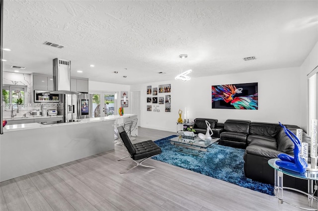 living room with a textured ceiling, visible vents, french doors, and light wood-type flooring