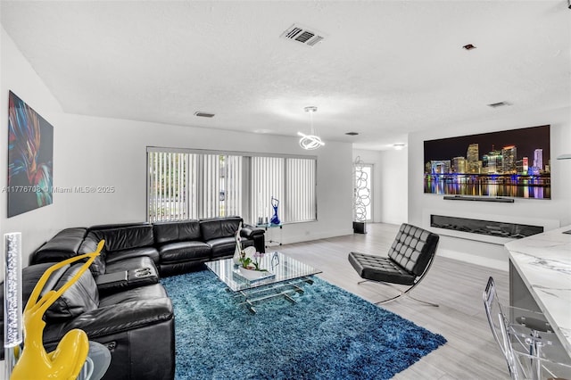 living room with a textured ceiling, light wood finished floors, and visible vents