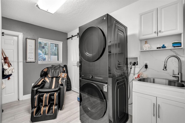 clothes washing area featuring a sink, light wood finished floors, a textured ceiling, stacked washer and clothes dryer, and cabinet space
