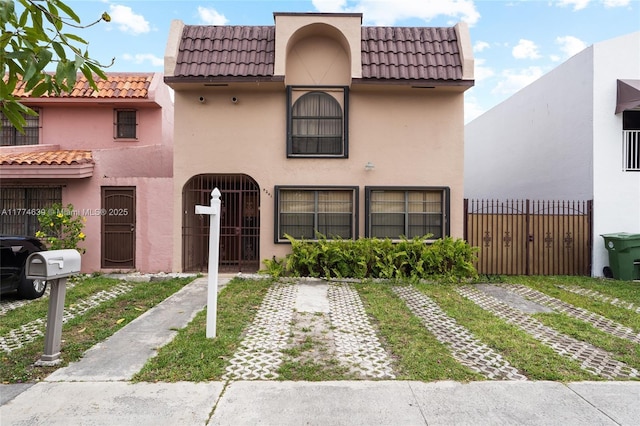 mediterranean / spanish-style house featuring stucco siding, a tiled roof, and fence