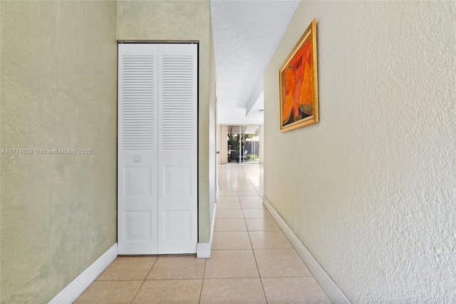 hall with a textured wall, baseboards, and light tile patterned flooring