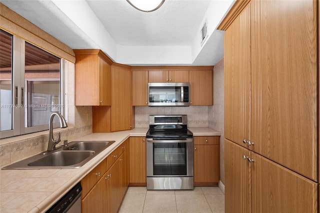 kitchen featuring light tile patterned floors, visible vents, a sink, stainless steel appliances, and decorative backsplash