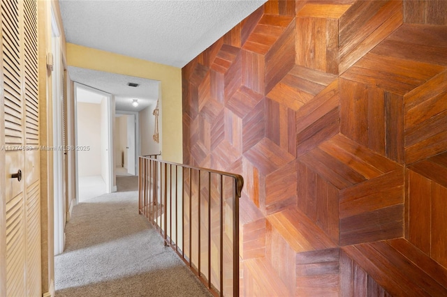 hall with carpet flooring, an upstairs landing, and a textured ceiling