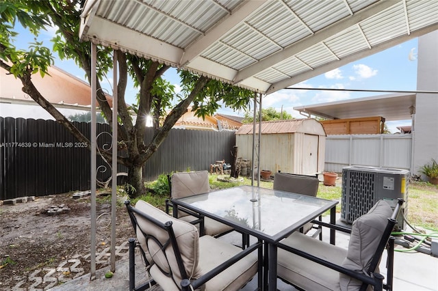 view of patio / terrace with central AC, a fenced backyard, outdoor dining area, a storage unit, and an outbuilding