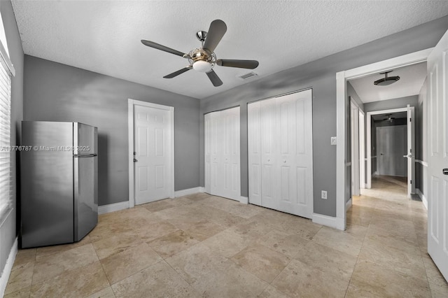 unfurnished bedroom with baseboards, visible vents, two closets, and freestanding refrigerator