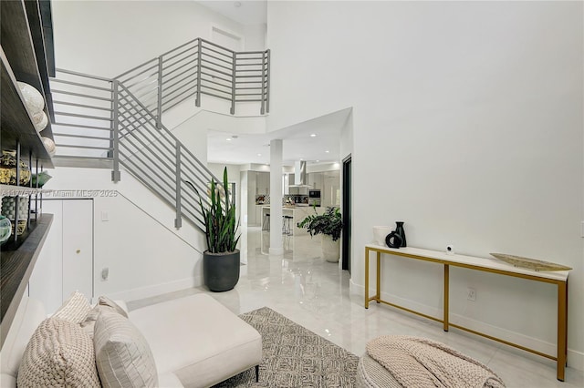 foyer entrance featuring marble finish floor, stairs, a towering ceiling, and baseboards