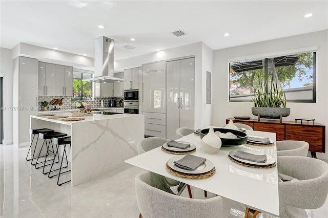 kitchen featuring a breakfast bar area, island range hood, gray cabinetry, modern cabinets, and black microwave