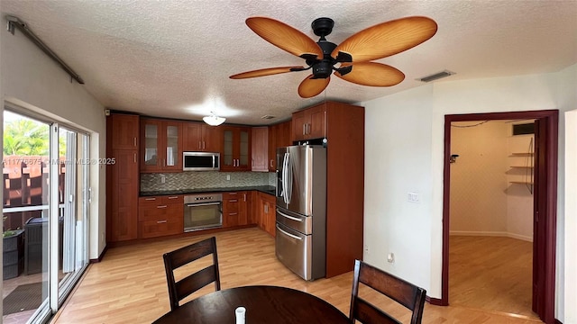 kitchen featuring tasteful backsplash, appliances with stainless steel finishes, glass insert cabinets, dark countertops, and visible vents