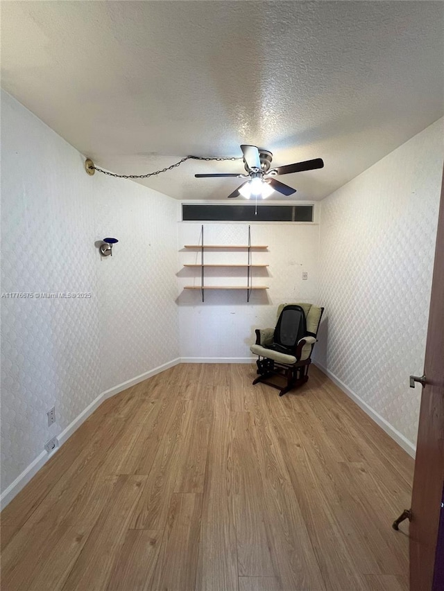 unfurnished room with baseboards, a textured ceiling, wallpapered walls, ceiling fan, and wood finished floors