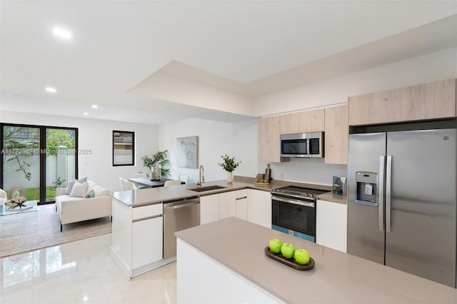 kitchen with modern cabinets, a peninsula, appliances with stainless steel finishes, a sink, and open floor plan