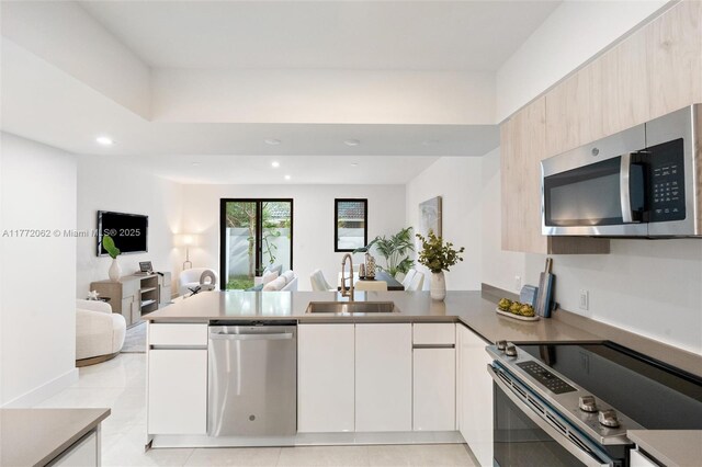 kitchen with recessed lighting, a peninsula, modern cabinets, stainless steel appliances, and a sink