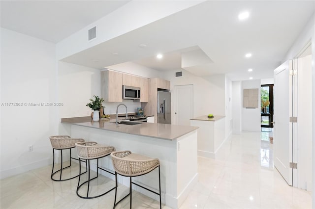 kitchen featuring baseboards, a peninsula, a breakfast bar area, appliances with stainless steel finishes, and a sink