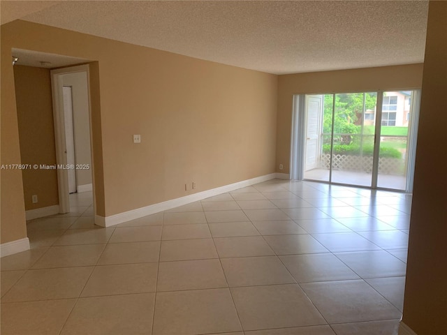 empty room with light tile patterned floors, baseboards, and a textured ceiling