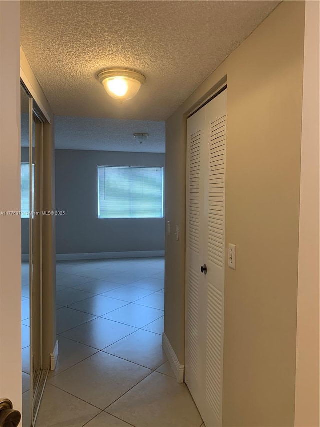 hallway with light tile patterned flooring, baseboards, and a textured ceiling
