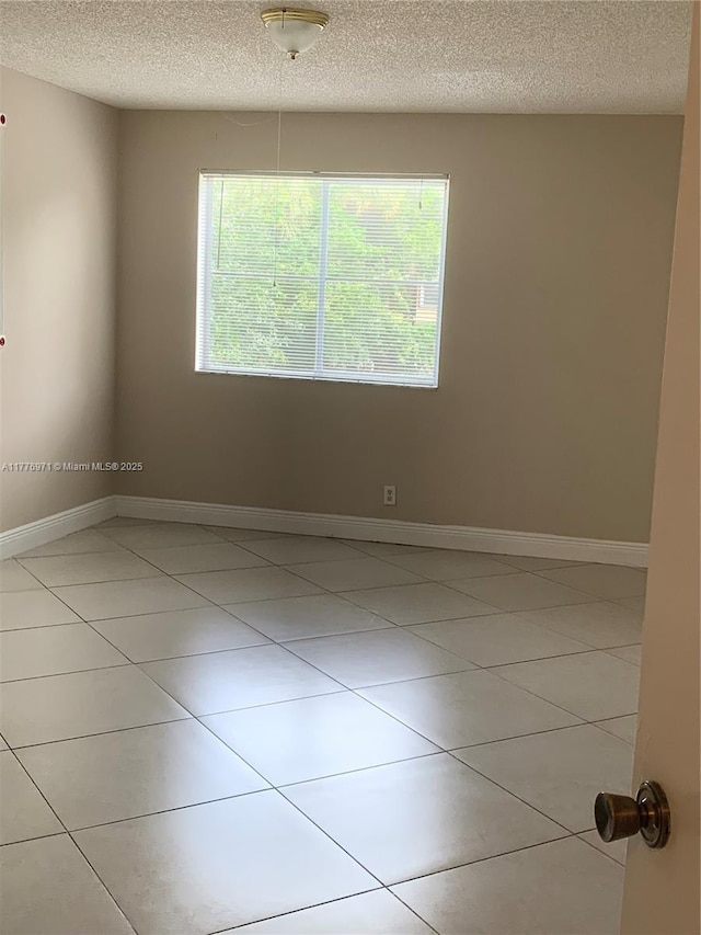 empty room with light tile patterned floors, baseboards, and a textured ceiling