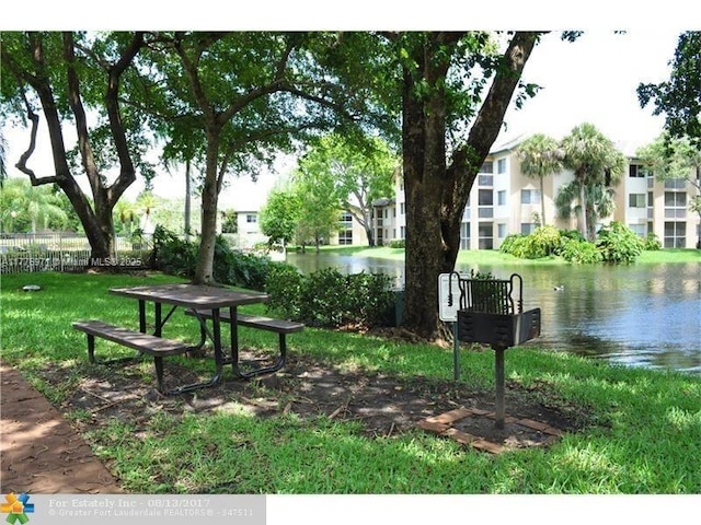 view of community with a yard, a water view, and fence