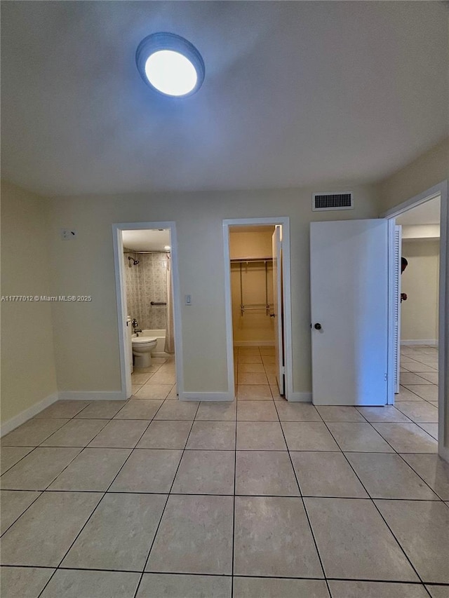 unfurnished bedroom with connected bathroom, a closet, a spacious closet, light tile patterned floors, and visible vents