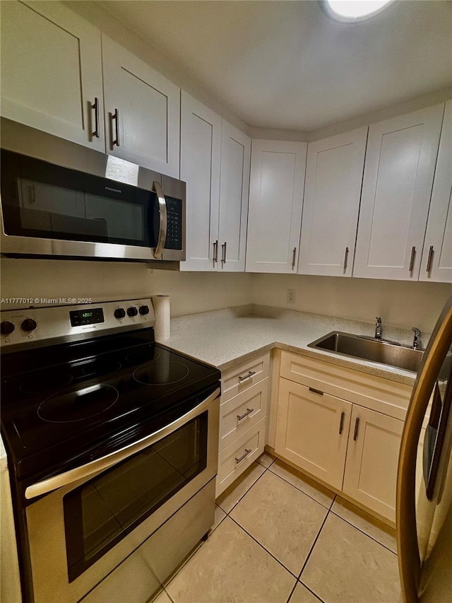 kitchen featuring light countertops, a sink, light tile patterned floors, stainless steel appliances, and white cabinets