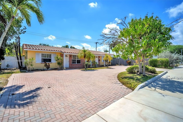 1910 NE 56th St, Fort Lauderdale, FL 33308 - ranch-style house featuring a tiled roof, fence, curved driveway, and stucco siding