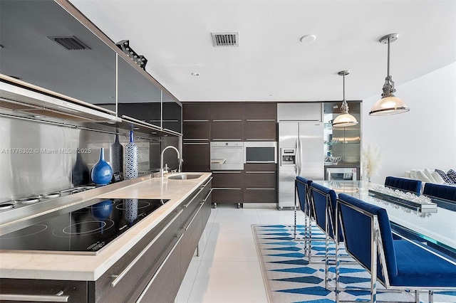 kitchen featuring visible vents, modern cabinets, stainless steel fridge, black electric cooktop, and a sink