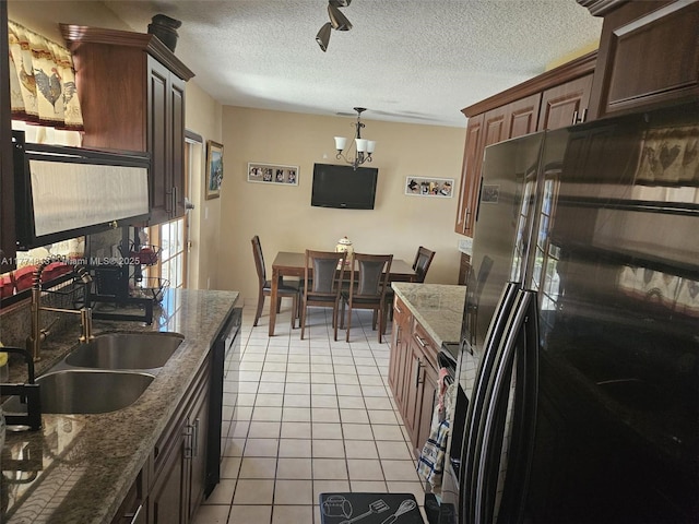 kitchen with black fridge, a textured ceiling, a sink, light tile patterned flooring, and dishwasher