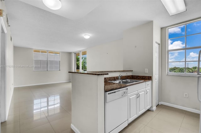 kitchen featuring light tile patterned flooring, white cabinets, a peninsula, a sink, and white dishwasher