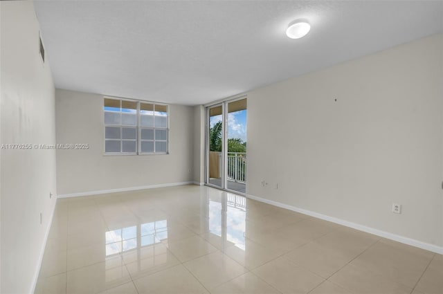 empty room with baseboards, expansive windows, visible vents, and tile patterned floors