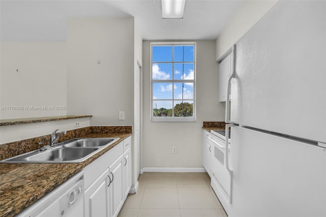kitchen with a sink, baseboards, light tile patterned floors, white appliances, and white cabinets