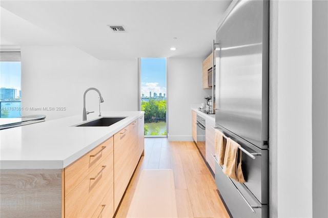 kitchen with light brown cabinetry, modern cabinets, a sink, a view of city, and stainless steel appliances