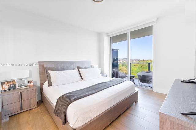 bedroom featuring expansive windows, light wood finished floors, and access to exterior