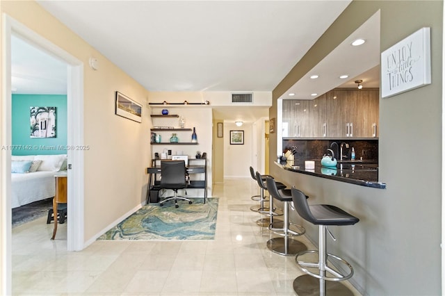 kitchen with baseboards, backsplash, dark countertops, visible vents, and a breakfast bar area