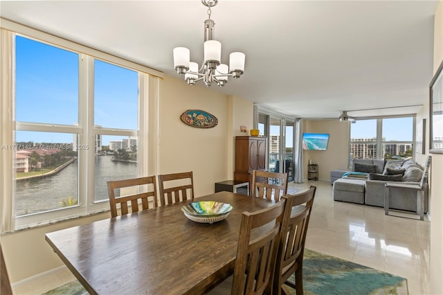dining space featuring ceiling fan with notable chandelier, tile patterned flooring, a wall of windows, and a water view