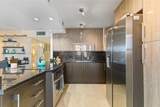 kitchen featuring dark stone counters, visible vents, appliances with stainless steel finishes, a sink, and decorative backsplash