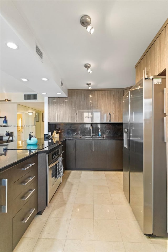 kitchen with modern cabinets, dark stone countertops, a sink, stainless steel appliances, and decorative backsplash