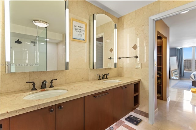 bathroom featuring a shower, double vanity, a sink, and tile walls